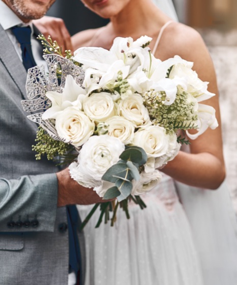 A bride and groom hold a bouquet of white roses