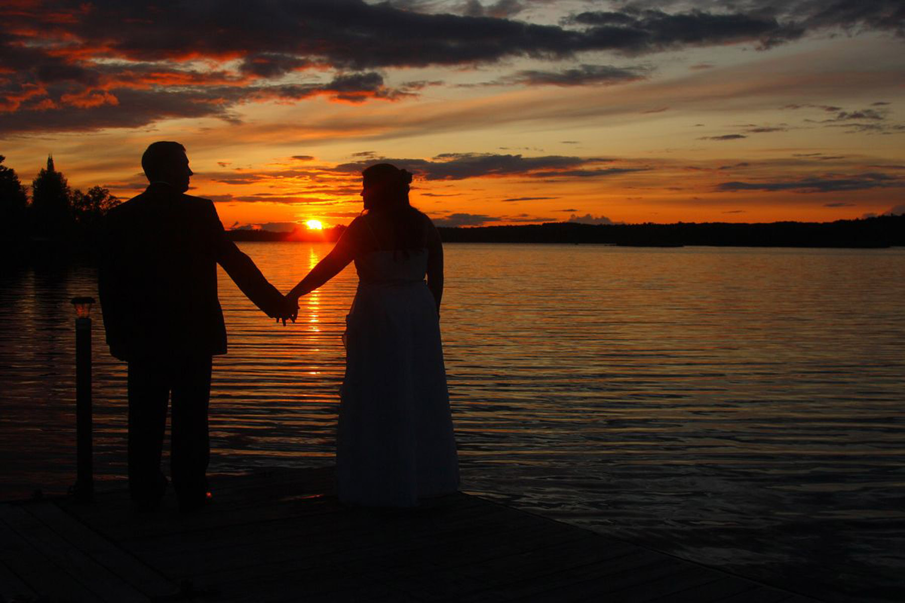 Newlywed couple facing Shagawa lake at sunset with backs to the camera.